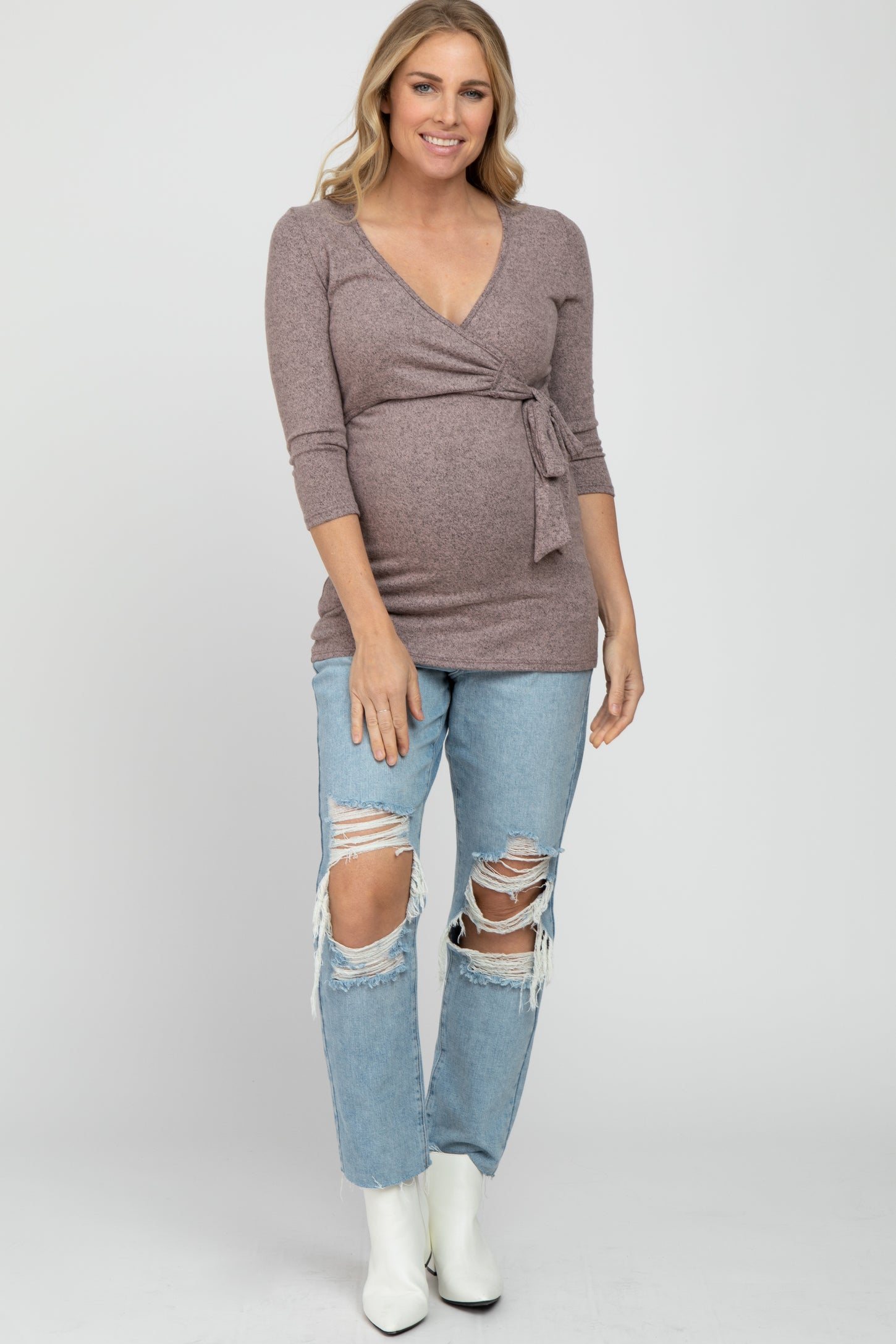 smiling pregnant woman wearing a mauve wrap maternity top and distressed blue jeans