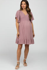 woman wearing a mauve maternity dress with flutter sleeves and a ruffled hem, showing her baby bump