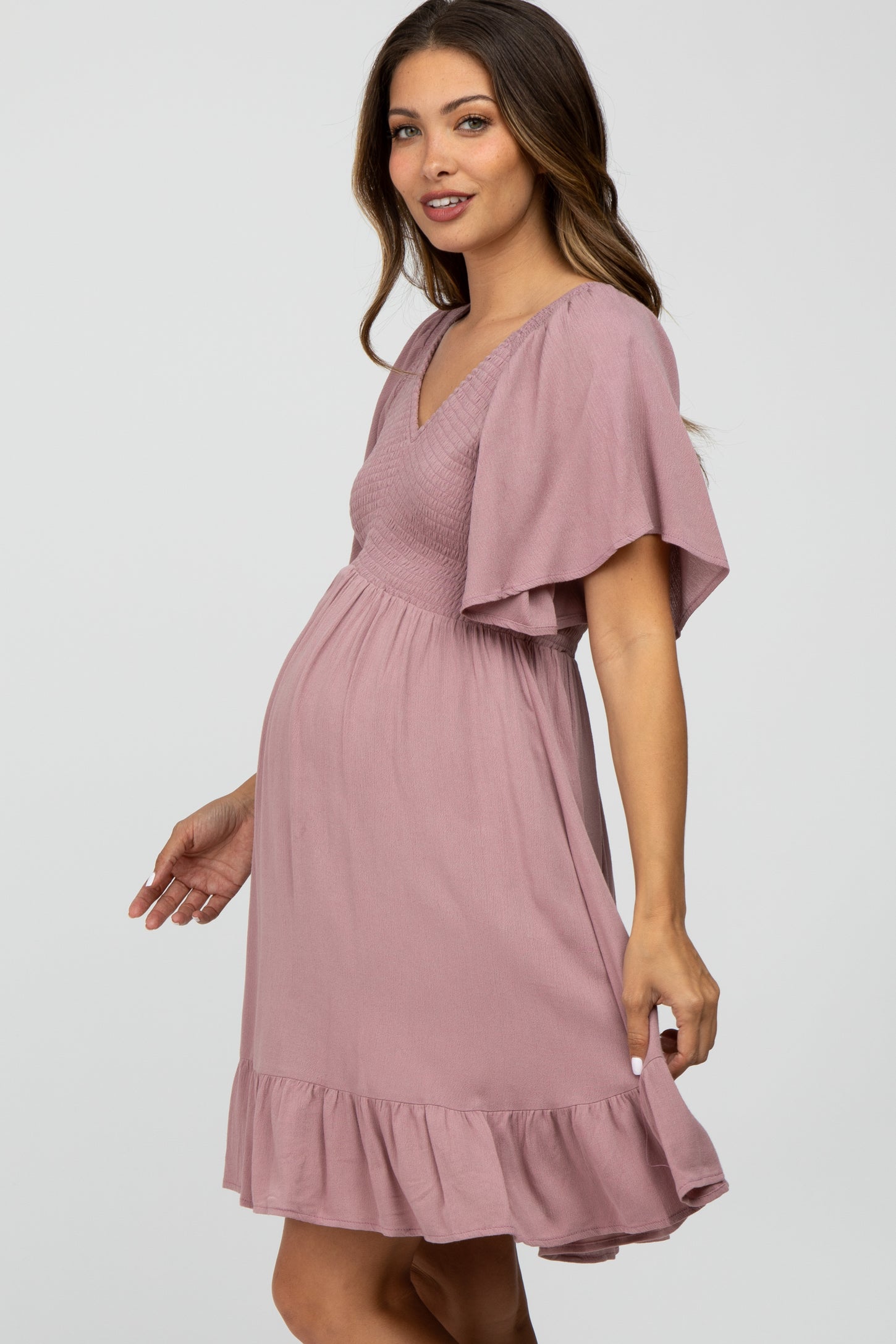 woman wearing a dusty rose maternity dress with short flutter sleeves and a ruffled hem, highlighting her baby bump