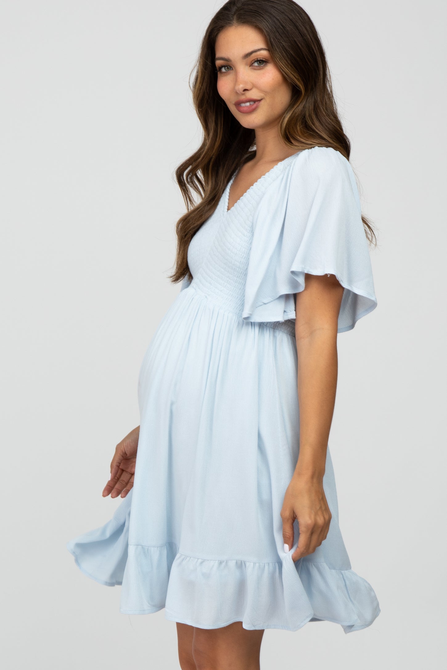 woman wearing a light blue maternity dress with flutter sleeves and a ruffled hemline, showcasing her baby bump
