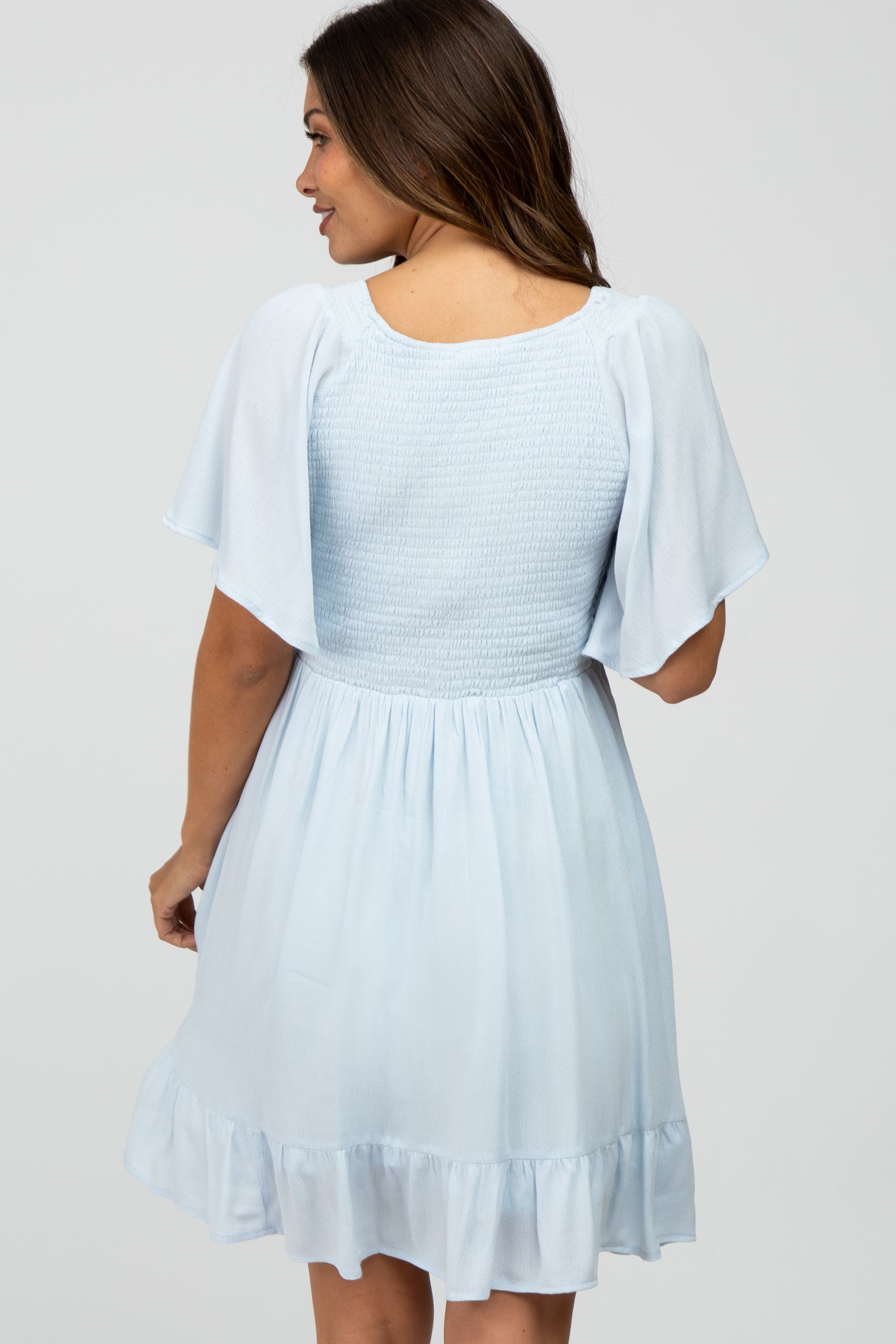woman wearing a light blue maternity dress with short flutter sleeves and a ruffled hem, showing a relaxed fit