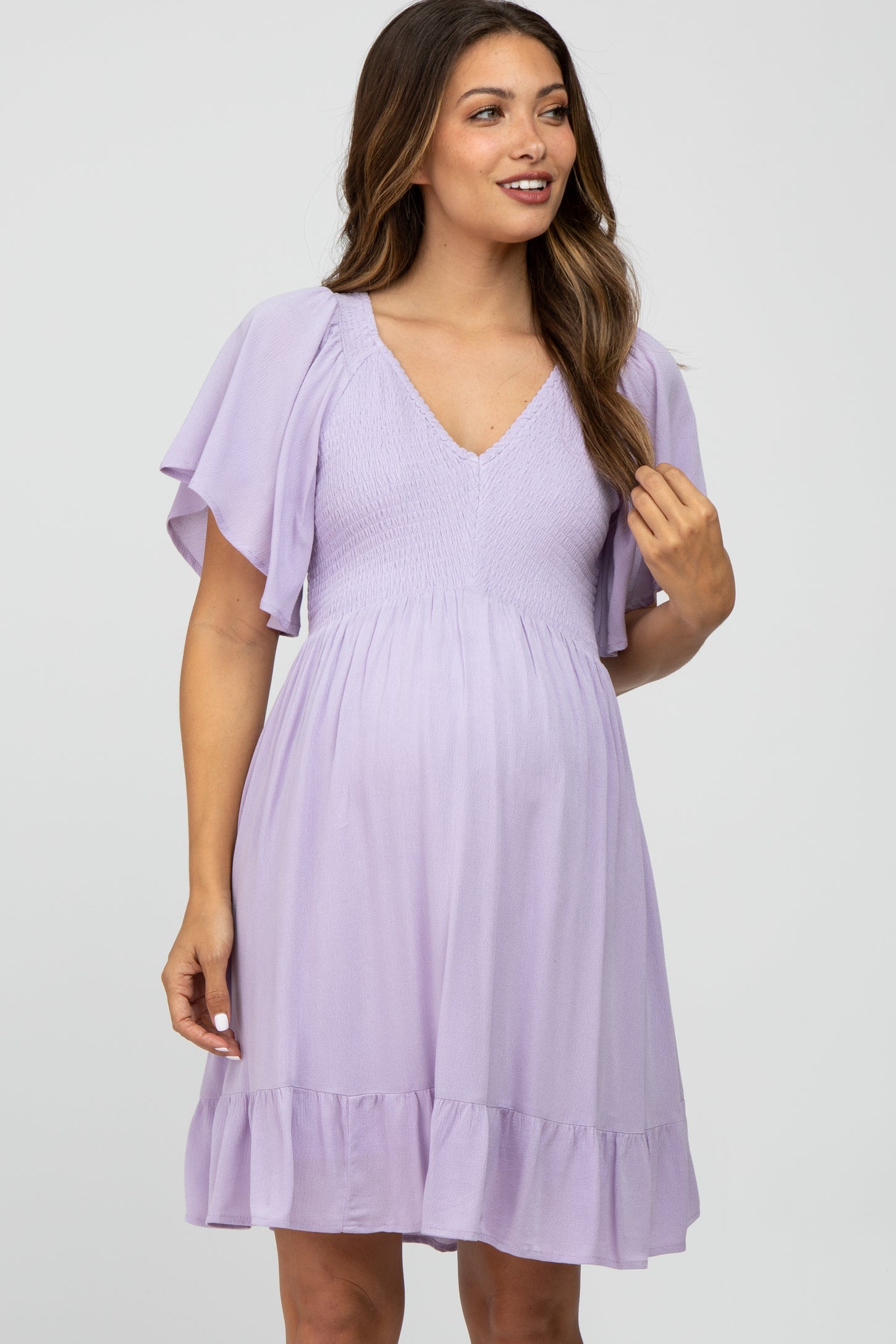 woman wearing a lavender maternity dress with flutter sleeves and a smocked bodice, showing off her baby bump