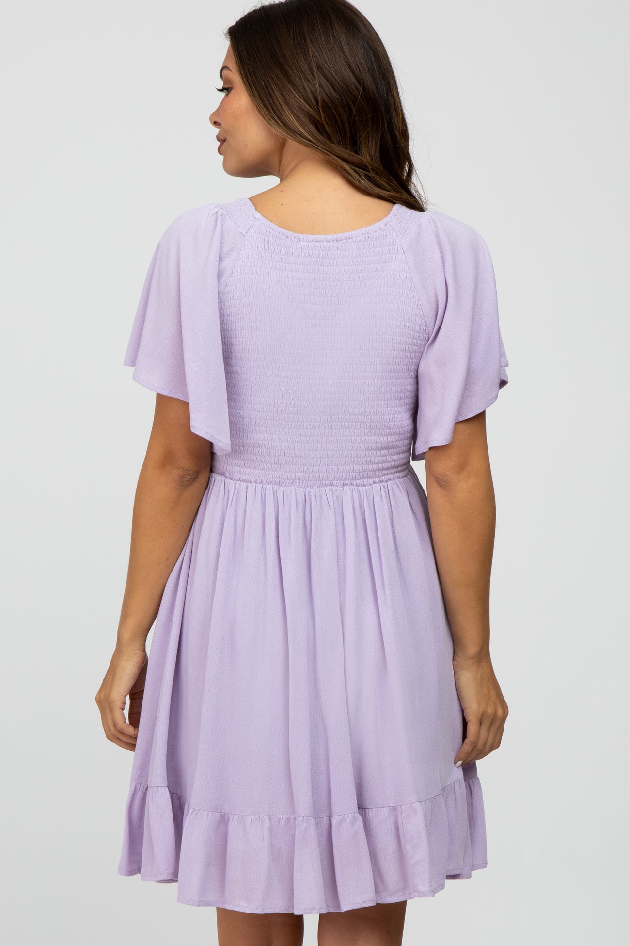 woman wearing a lavender short sleeve maternity dress with a smocked bodice and ruffle hem, seen from the back