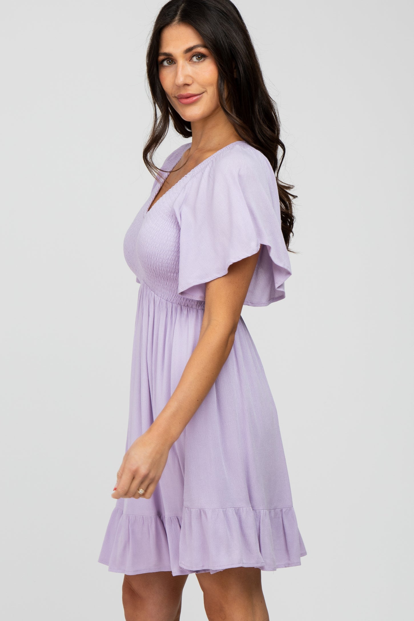 woman wearing a lavender short sleeve dress with ruffled hem and a fitted bodice, smiling to the side