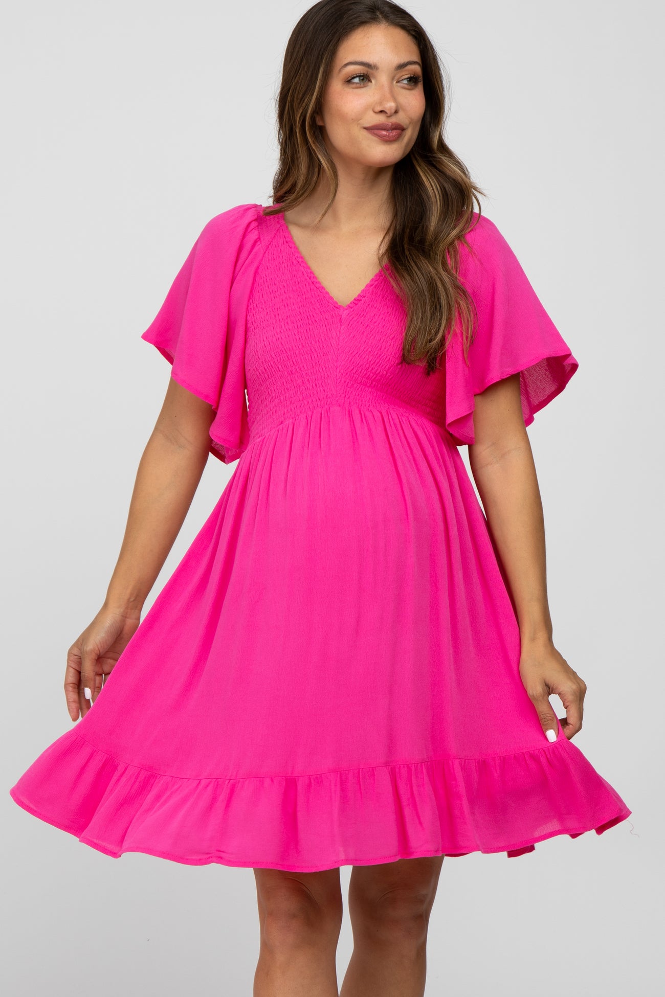 woman wearing a bright pink maternity dress with flutter sleeves and a tiered ruffle hem, showcasing her baby bump