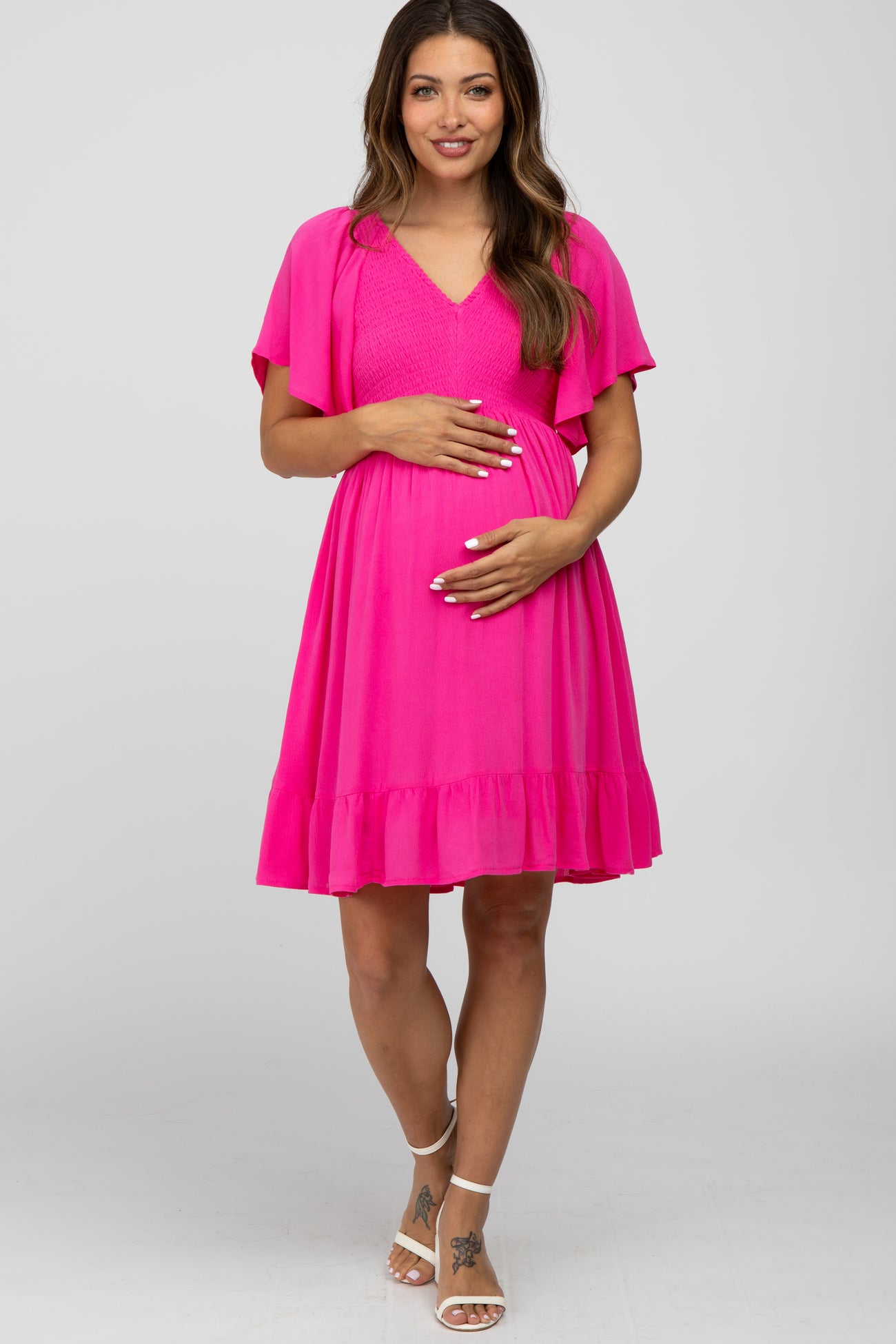 woman wearing a bright pink maternity dress with flutter sleeves and a ruffled hem, holding her baby bump