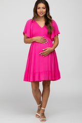 woman wearing a bright pink maternity dress with flutter sleeves and a ruffled hem, holding her baby bump
