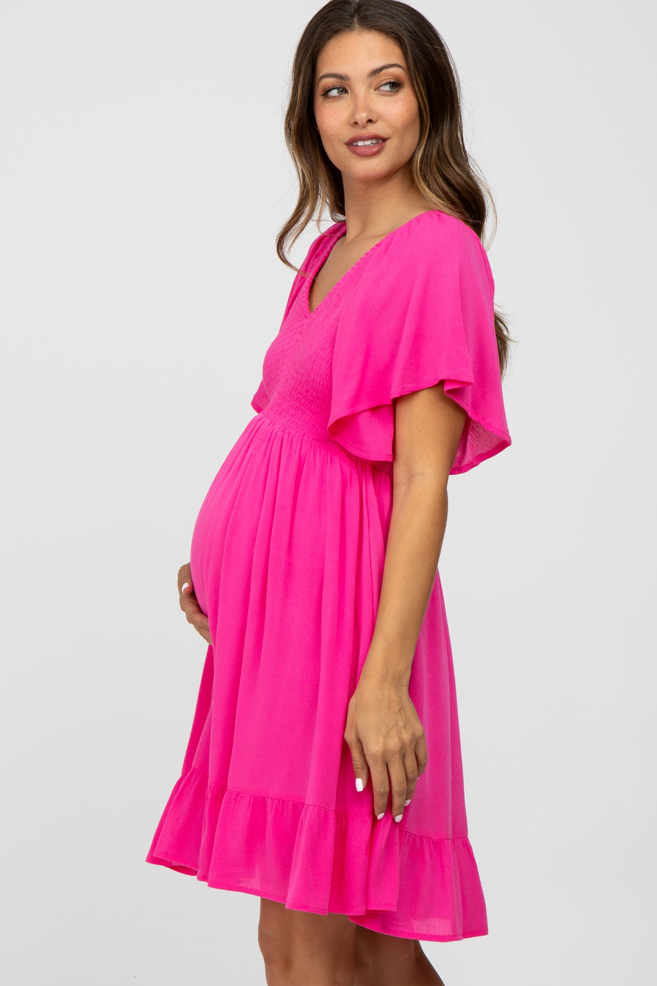 Pregnant woman wearing a bright pink maternity dress with flutter sleeves and a smocked bodice