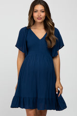 woman wearing a navy blue maternity dress with a smocked bodice and flutter sleeves, showcasing her baby bump