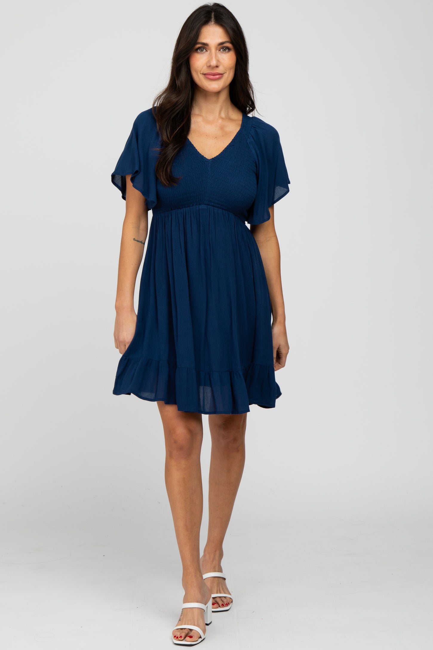woman wearing a navy blue short sleeve maternity dress with a smocked bodice and ruffle hem