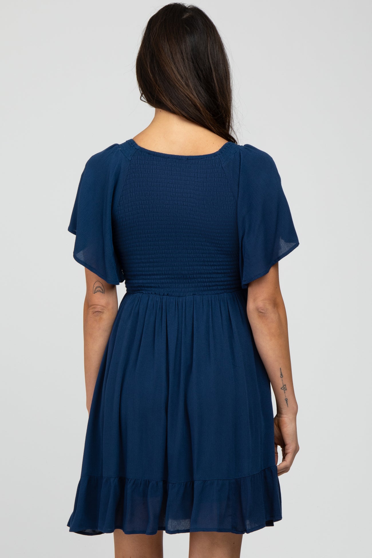 woman wearing a navy blue short sleeve dress with a smocked bodice and ruffled hemline, viewed from the back