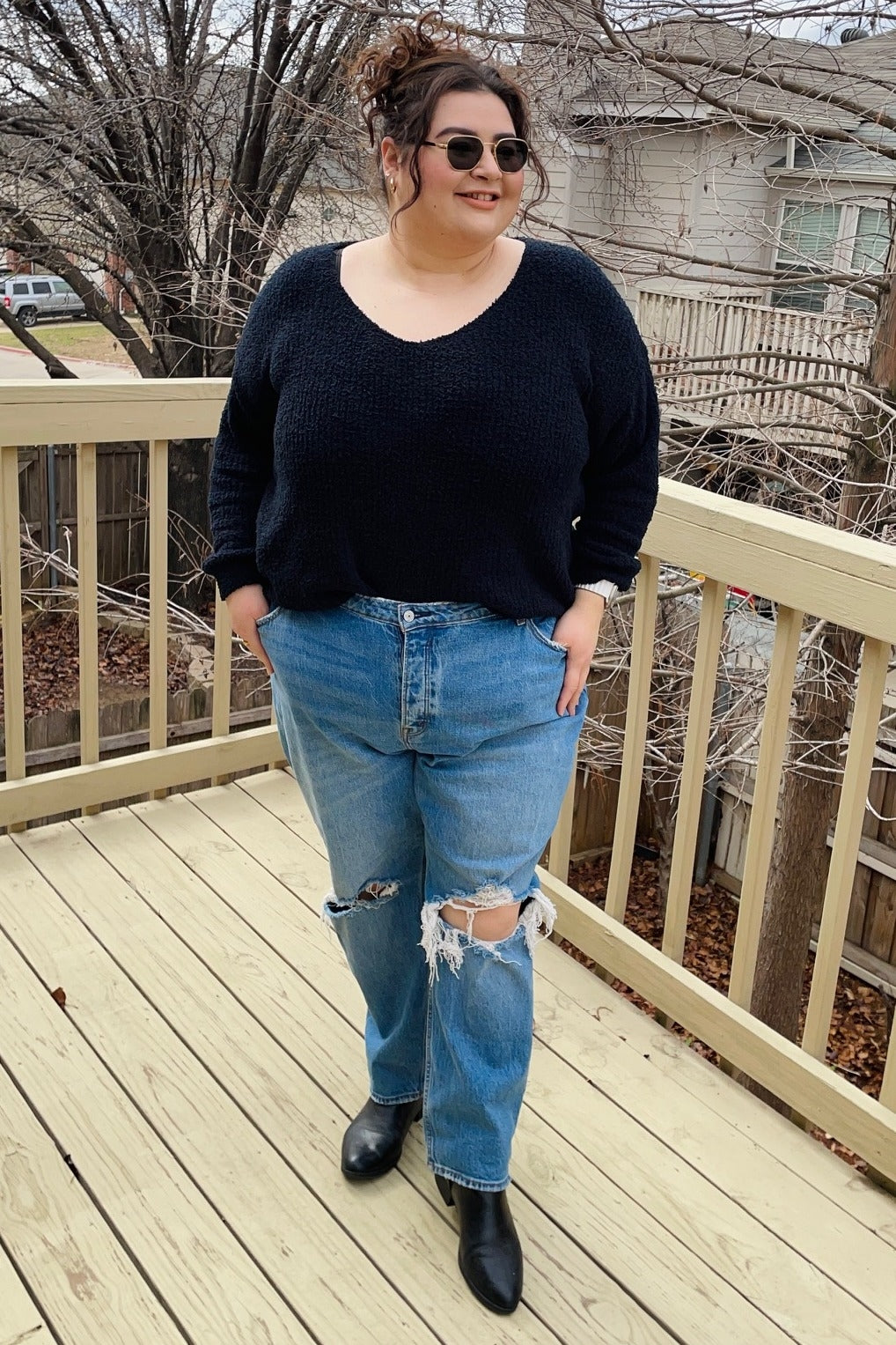 woman wearing a black oversized sweater and ripped light blue high-waisted jeans, standing on a deck outdoors
