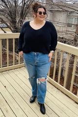 woman wearing a black oversized sweater and ripped light blue high-waisted jeans, standing on a deck outdoors