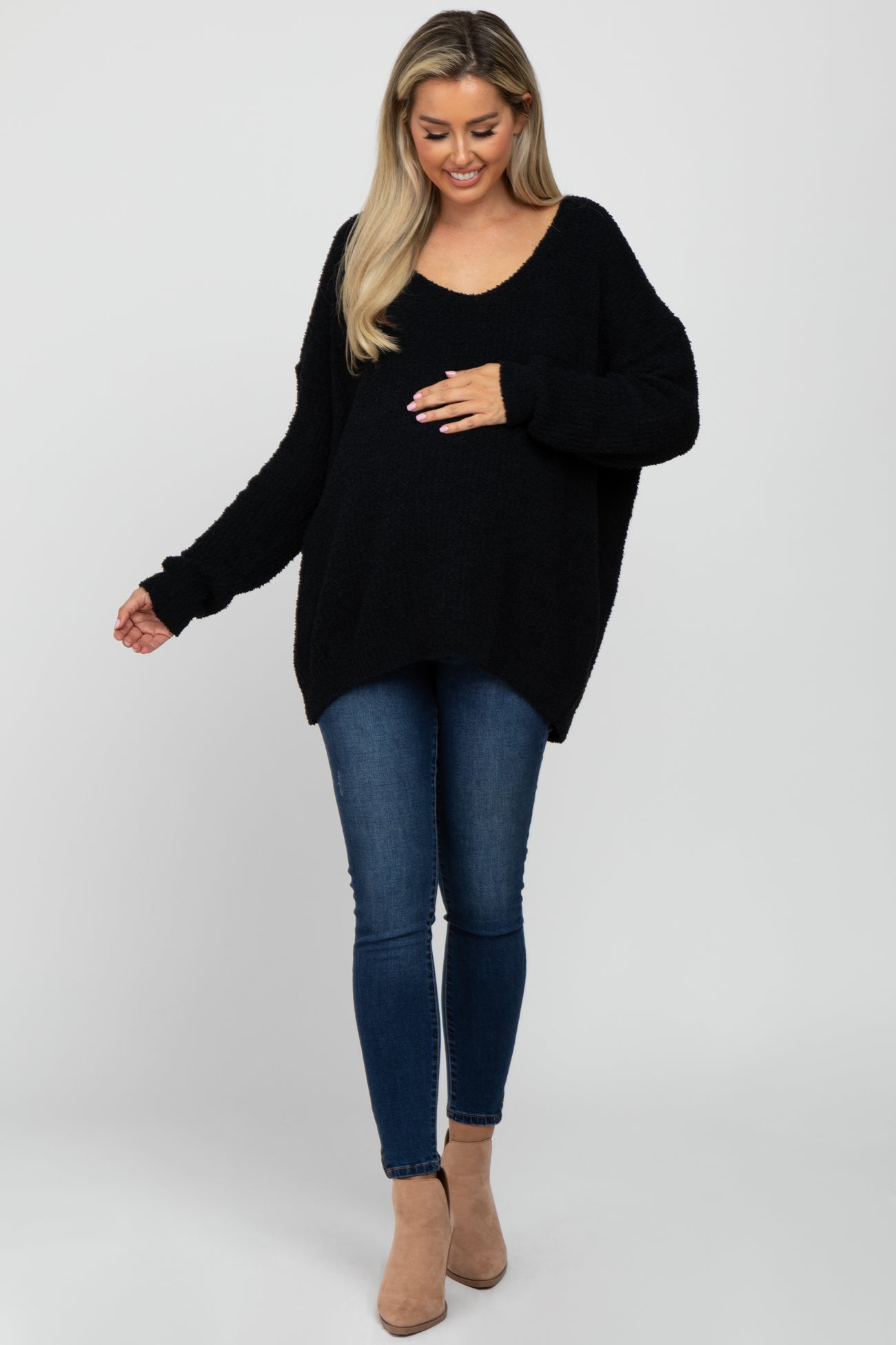 woman wearing a black oversized maternity sweater and blue skinny jeans, gently holding her baby bump