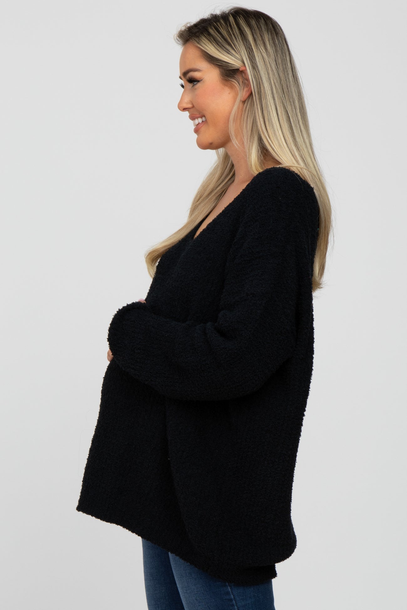 Blonde woman smiling in profile wearing an oversized black fuzzy knit sweater and blue jeans