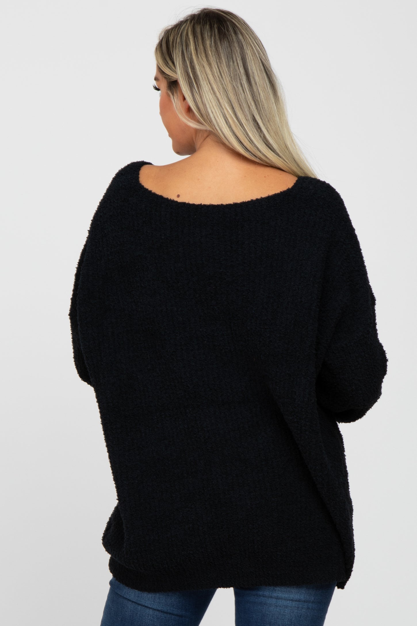 woman wearing a cozy black maternity sweater with an open back and relaxed fit, showing a slight baby bump