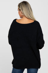 woman wearing a cozy black maternity sweater with an open back and relaxed fit, showing a slight baby bump