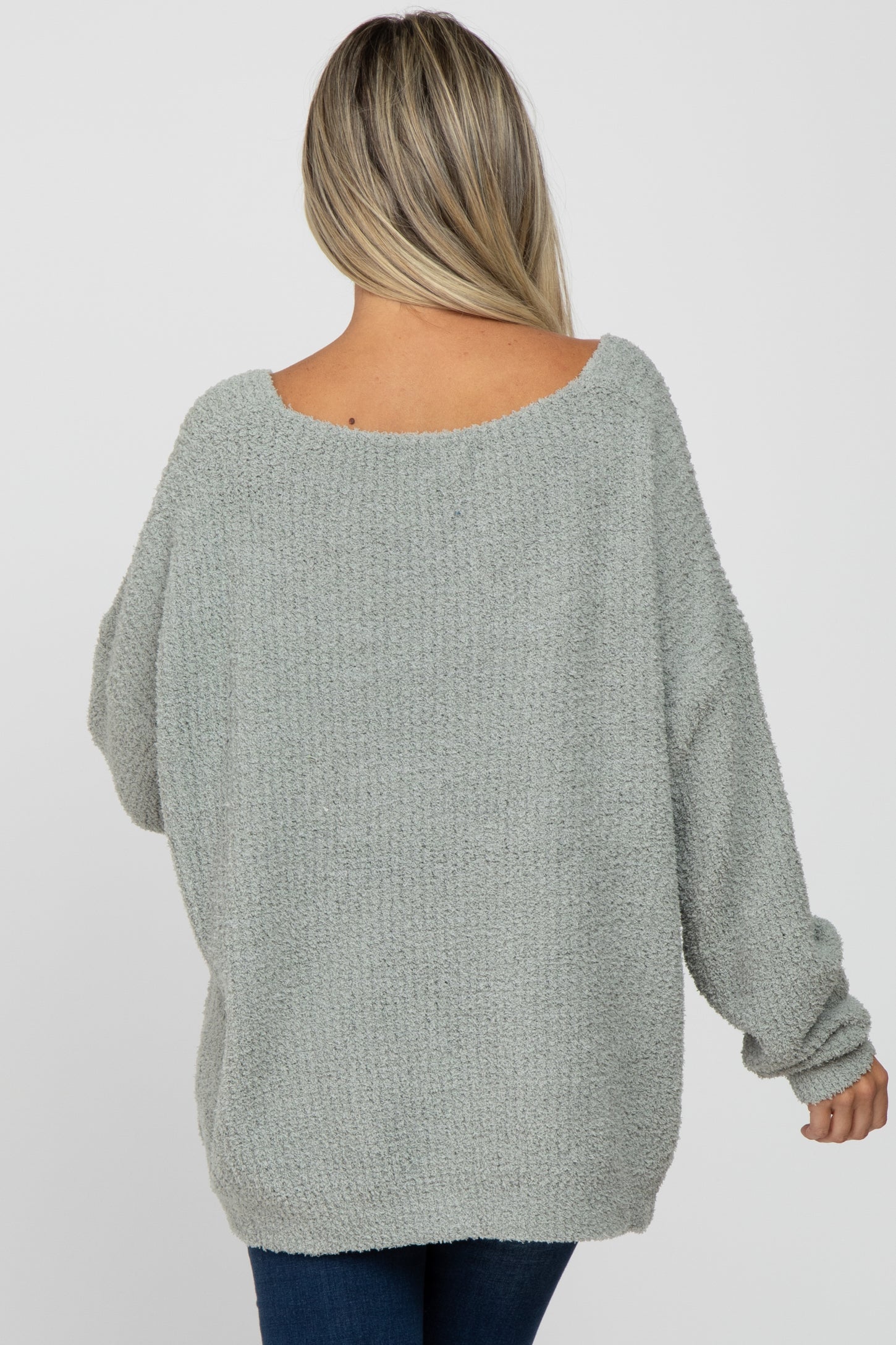 back view of a woman wearing an oversized light green fuzzy knit sweater and blue jeans
