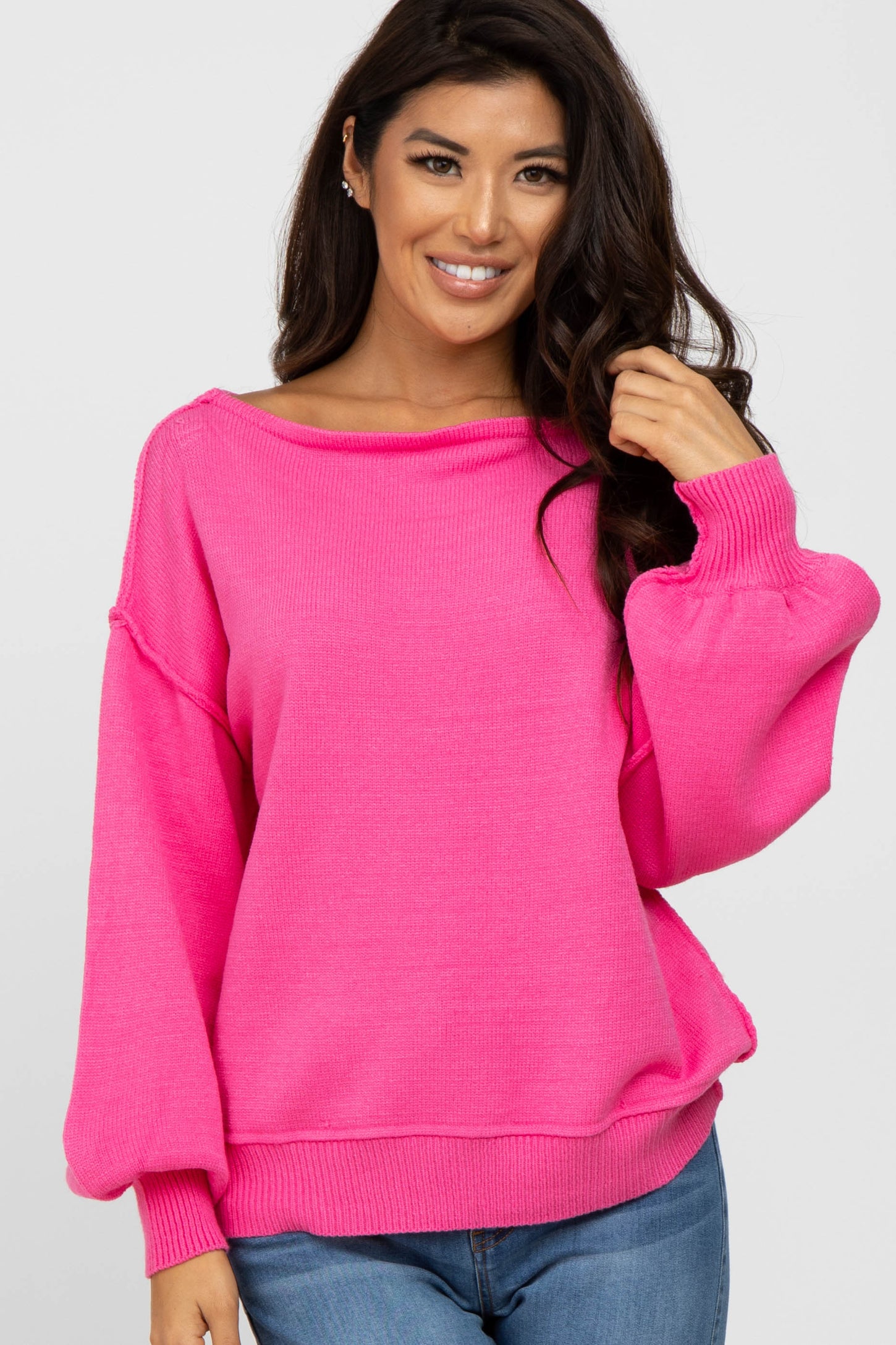 woman wearing a bright pink boat neck sweater with balloon sleeves and blue jeans