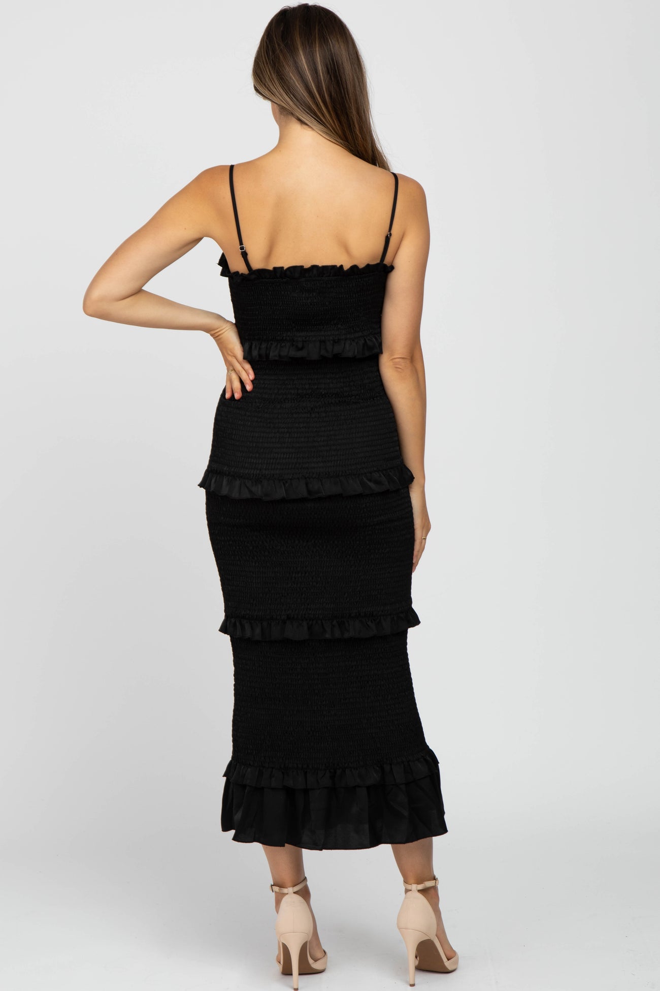 Back view of a woman wearing a black smocked tiered midi dress with spaghetti straps and beige heels