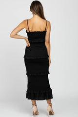 Back view of a woman wearing a black smocked tiered midi dress with spaghetti straps and beige heels