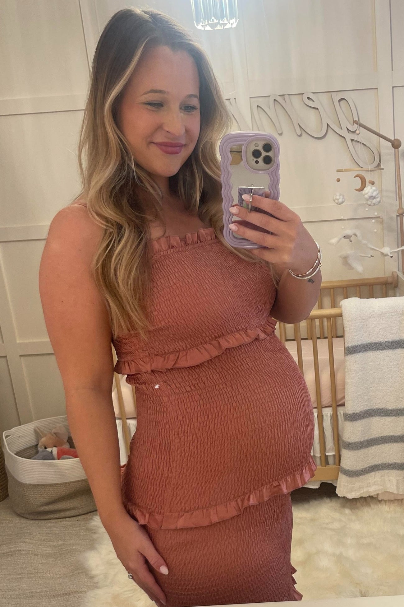 woman wearing a dusty rose maternity dress with ruffles, showing her baby bump while taking a selfie