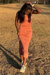 woman in orange smocked midi dress with ruffles posing in a grassy field at sunset