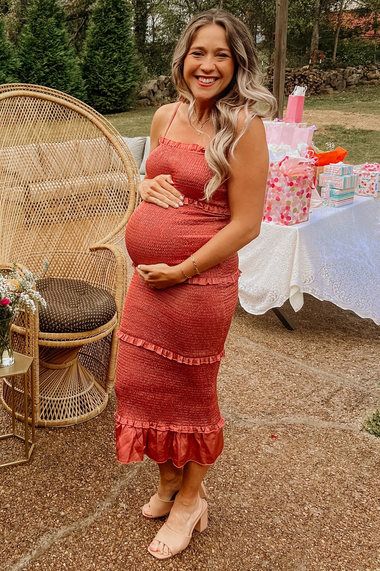 smiling pregnant woman in a rust-colored smocked midi dress at an outdoor baby shower with gifts