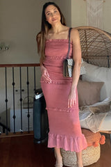 woman wearing a light pink strapless midi dress with ruffle details, standing next to a woven chair