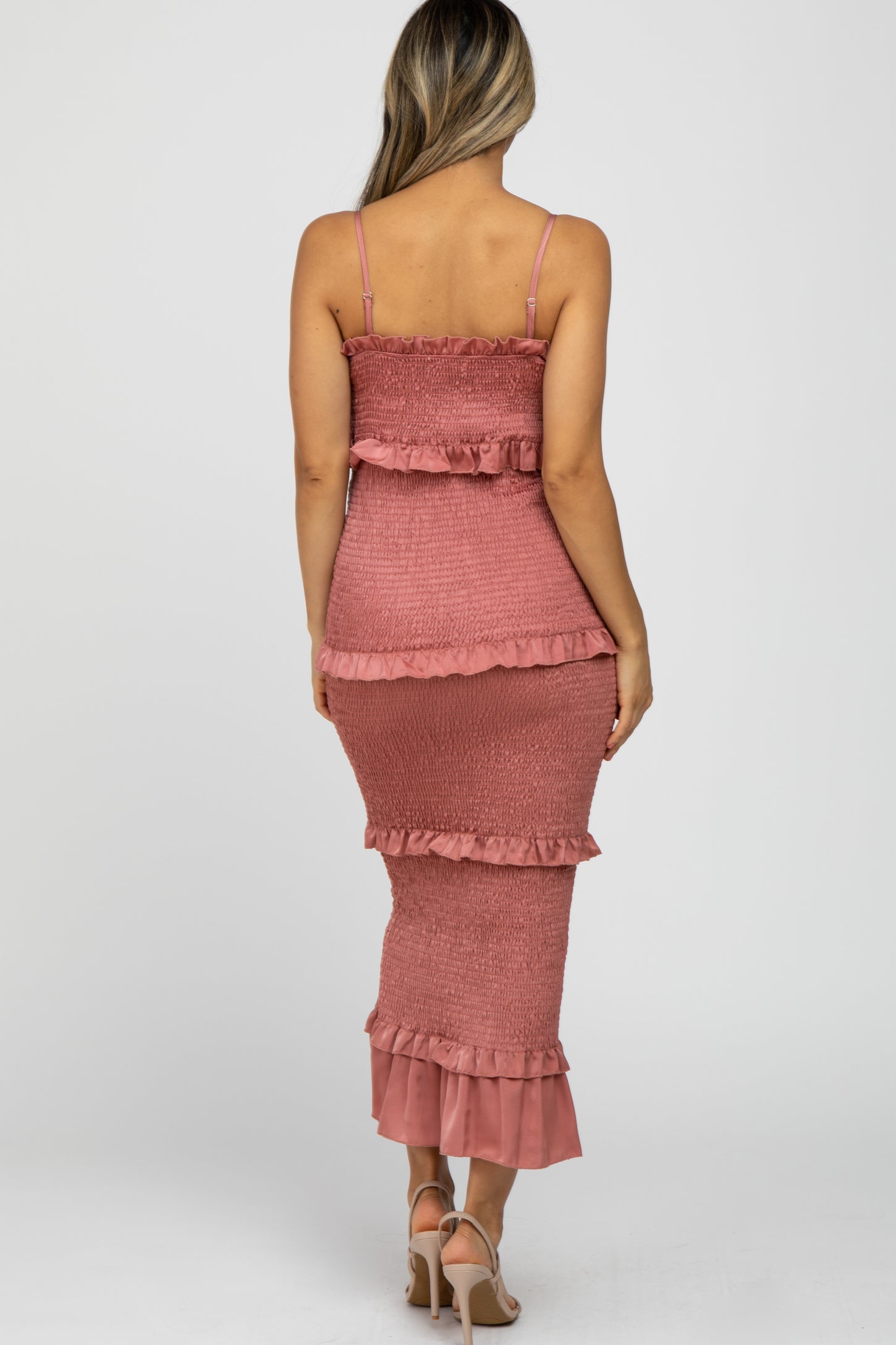 Back view of a woman wearing a mauve smocked tiered maternity maxi dress with ruffle details and spaghetti straps