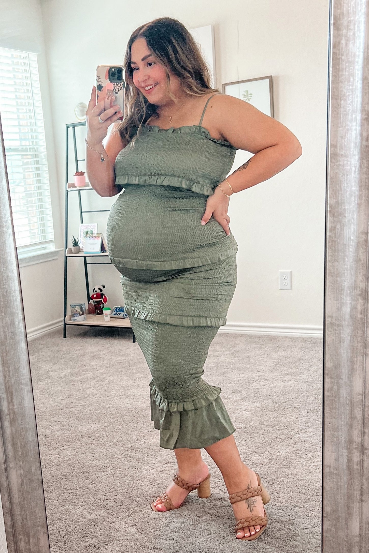 woman wearing a green maternity dress with ruffles and a visible baby bump, standing in front of a mirror