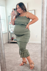 woman wearing a green maternity dress with ruffles and a visible baby bump, standing in front of a mirror