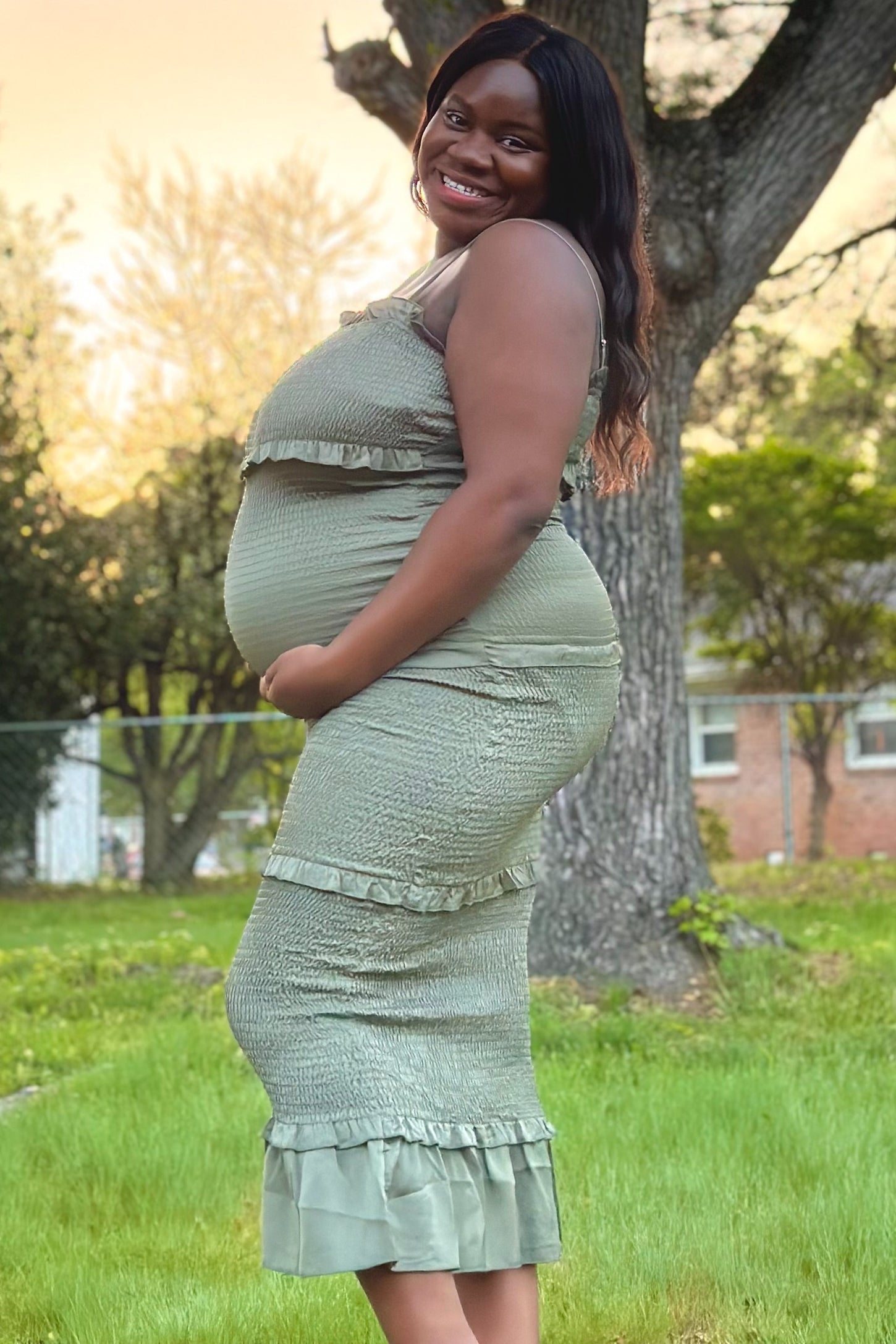 woman wearing a light green maternity dress with ruffle details, showcasing her baby bump while standing outside