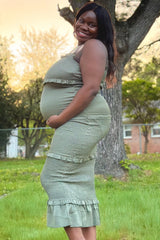 woman wearing a light green maternity dress with ruffle details, showcasing her baby bump while standing outside