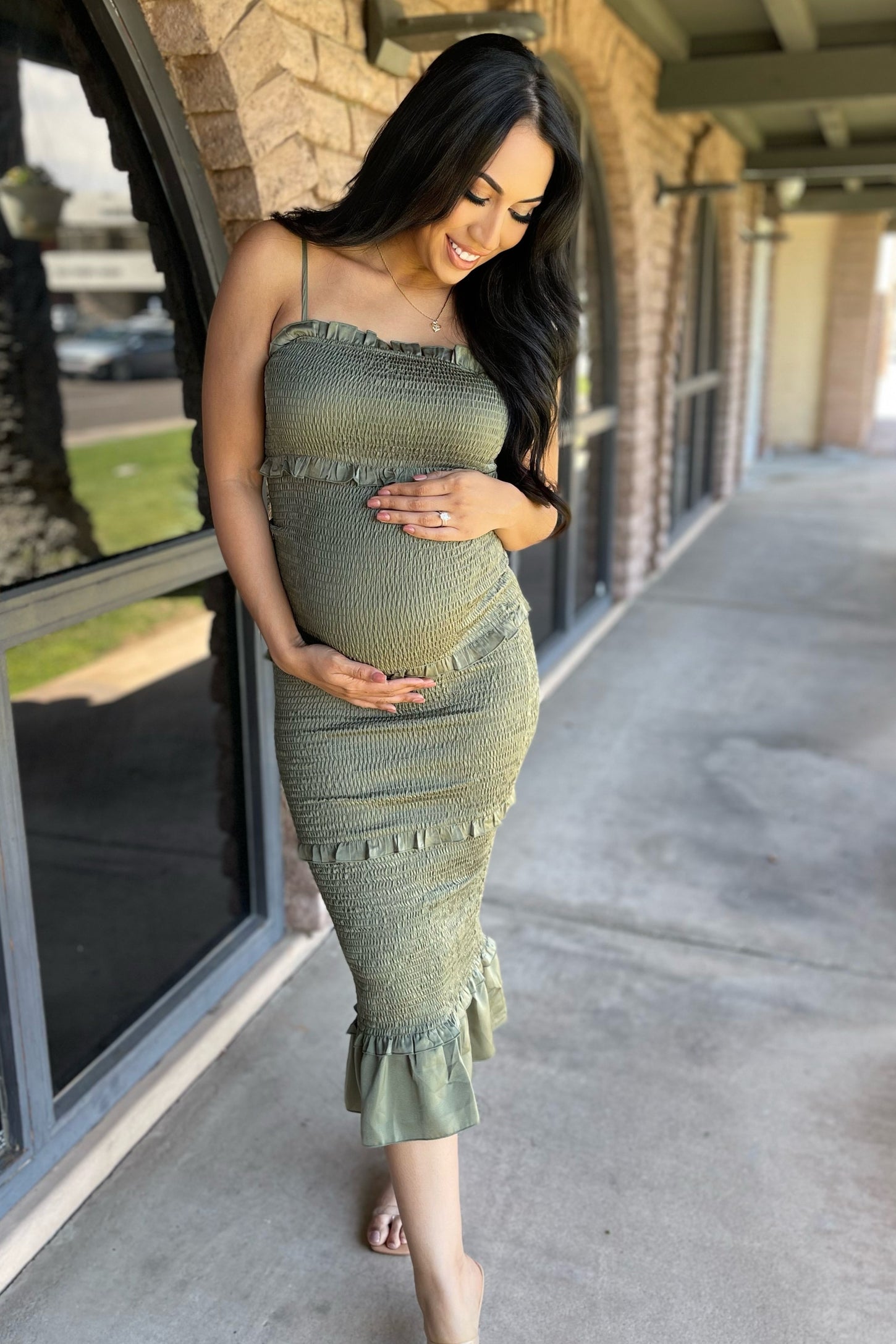 woman wearing a light olive green maternity dress with ruffle details and a visible baby bump