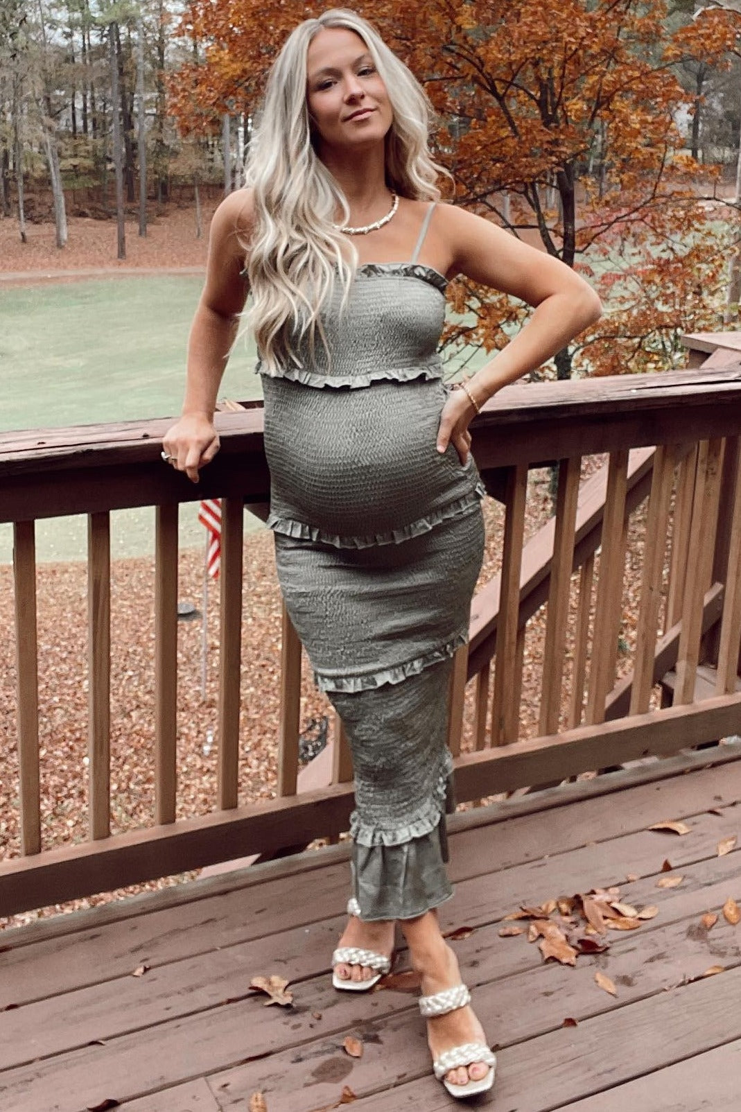 woman wearing a green maternity dress with ruffles and spaghetti straps, showing off her baby bump on a wooden deck