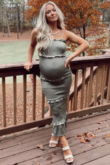 woman wearing a green maternity dress with ruffles and spaghetti straps, showing off her baby bump on a wooden deck