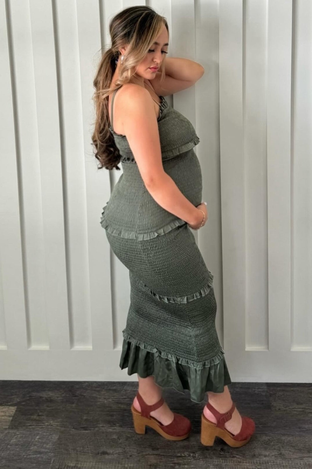 woman wearing a green smocked maternity dress with ruffle details, showing her baby bump