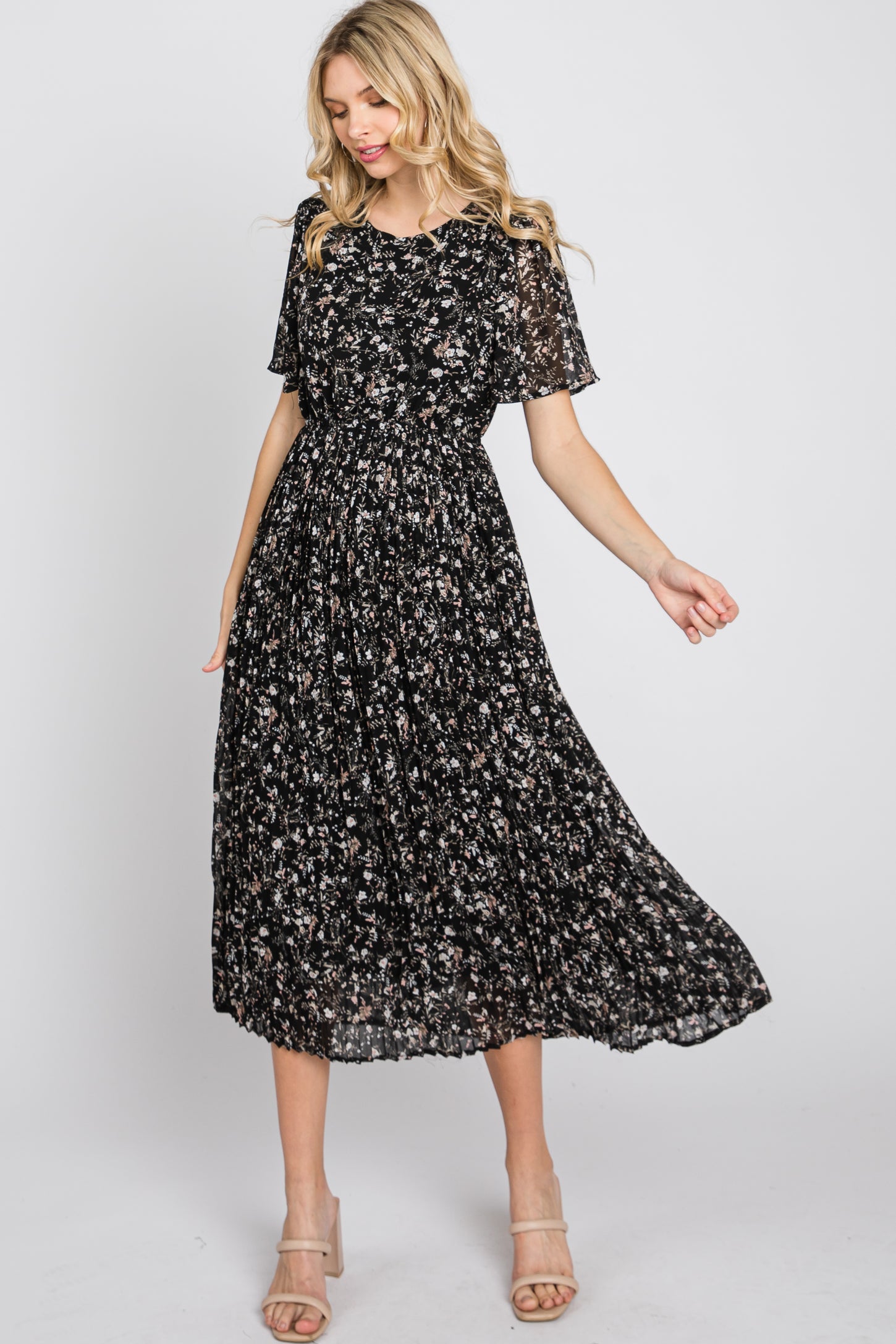 woman wearing a black floral midi dress with short sleeves and a smocked bodice, styled with strappy heels