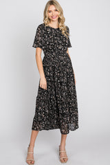 woman wearing a black floral print midi dress with short sleeves and a cinched waist