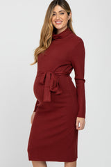 smiling pregnant woman wearing a burgundy ribbed turtleneck maternity dress with a waist tie
