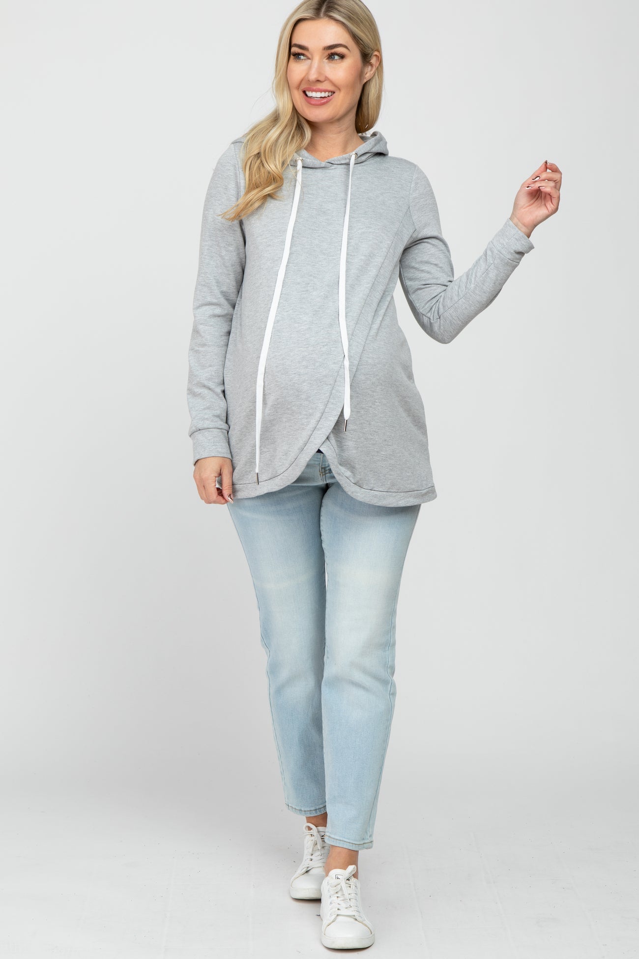 woman wearing a gray maternity hoodie with a drawstring and a baby bump visible, paired with light wash jeans