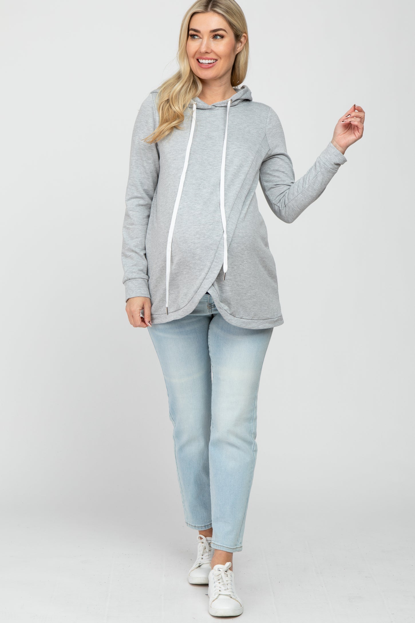 woman wearing a gray maternity hoodie with a drawstring and a baby bump visible, paired with light wash jeans
