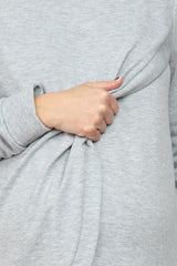 woman wearing a light gray maternity top with a knotted detail at the hip and a visible baby bump