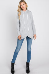 woman wearing a gray oversized hoodie with a curved hem and white drawstrings, paired with blue skinny jeans and black ankle boots