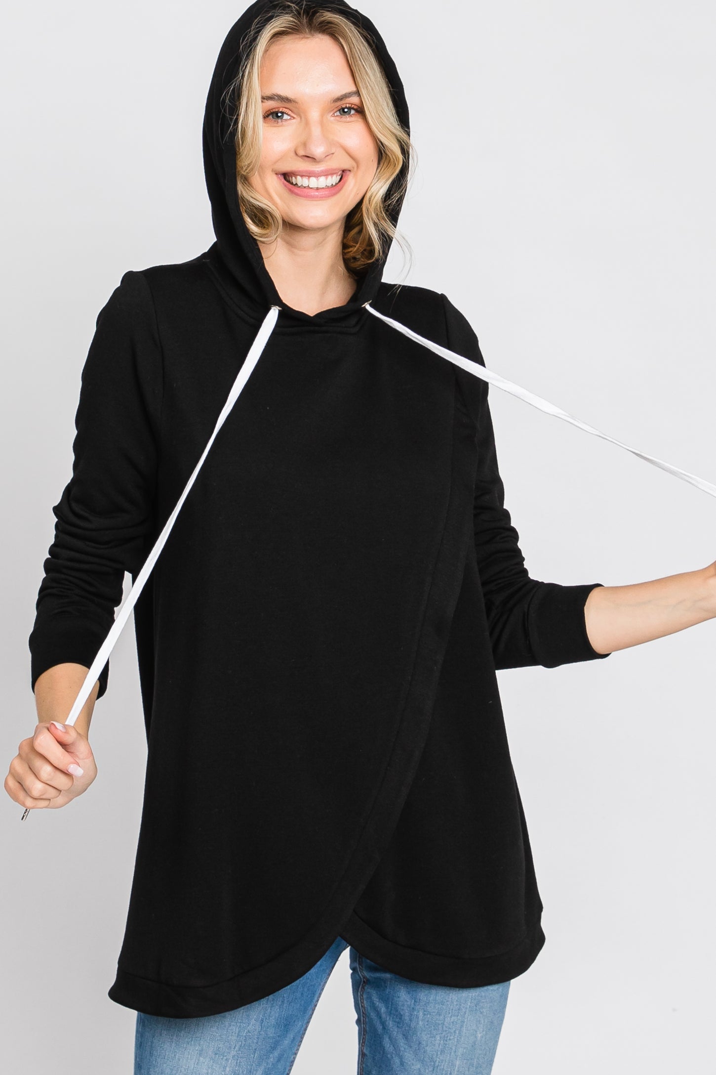 smiling woman wearing a black nursing hoodie with white drawstrings and tulip hem over blue jeans