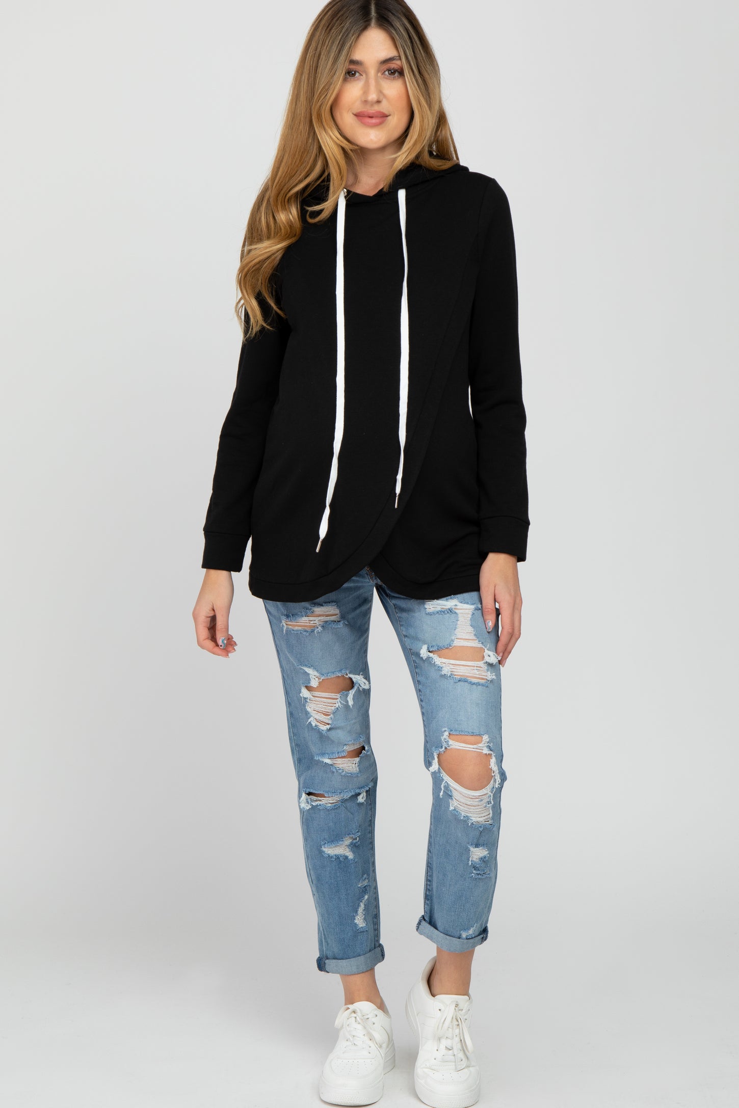 woman wearing a black maternity hoodie with a wrap design, paired with distressed light blue jeans and white sneakers