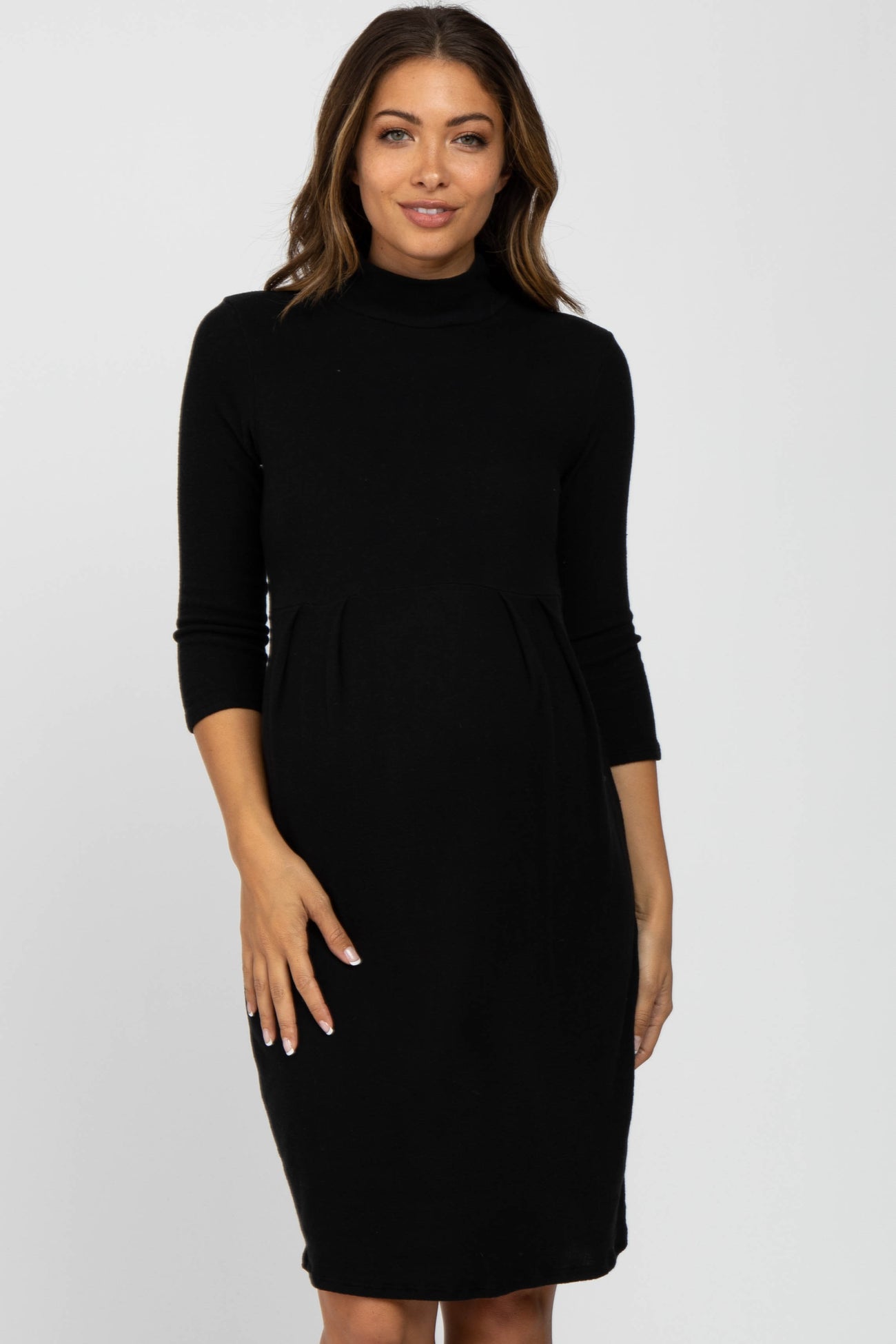 Pregnant woman wearing a black long-sleeve turtleneck maternity dress against a white background