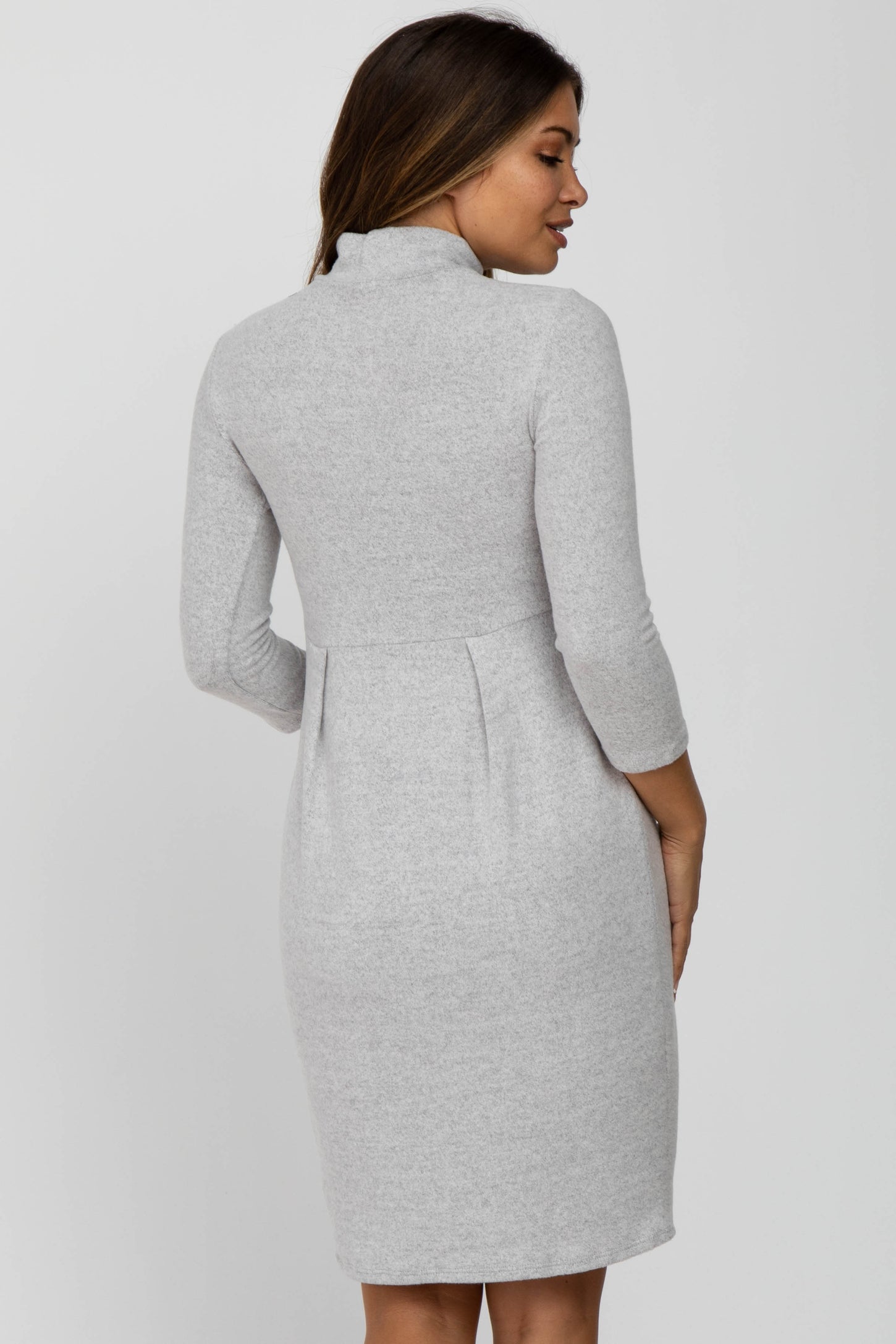 back view of woman wearing a grey long sleeve knit maternity dress with a high neckline