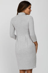 back view of woman wearing a grey long sleeve knit maternity dress with a high neckline
